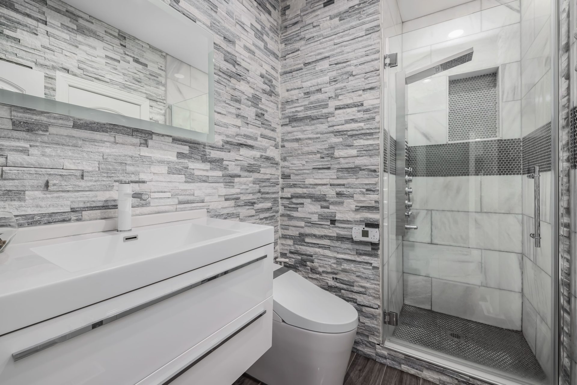 Stilvolles, modernes Badezimmer mit Glasdusche, Steinwänden und einem schlichten weißen Waschtisch.