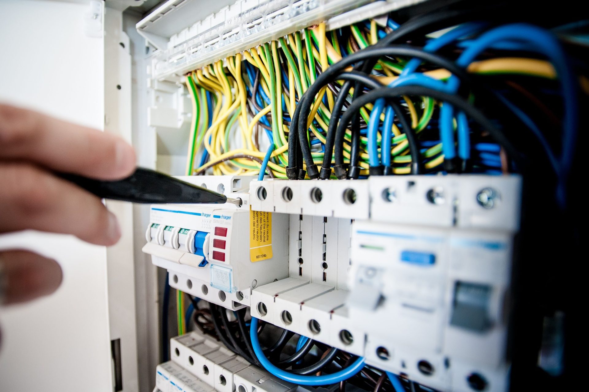 Die Hand eines Elektrikers arbeitet an einem Sicherungskasten mit bunten Drähten und sorgt für sichere elektrische Verbindungen.